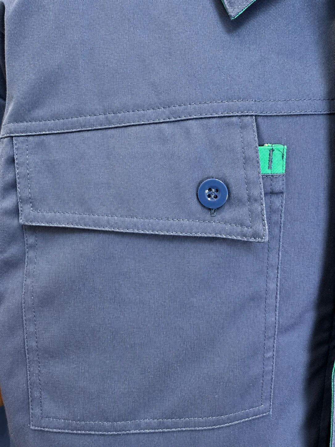 Blue workwear chest pocket with a matching button, green contrast tab and visible topstitching